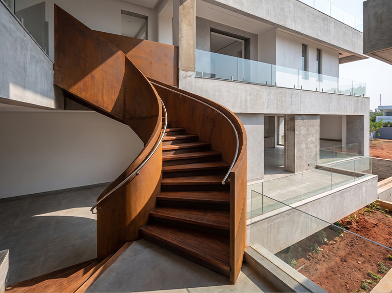 Escalier métallique courbe aspect Corten avec marches en bois dans une villa contemporaine